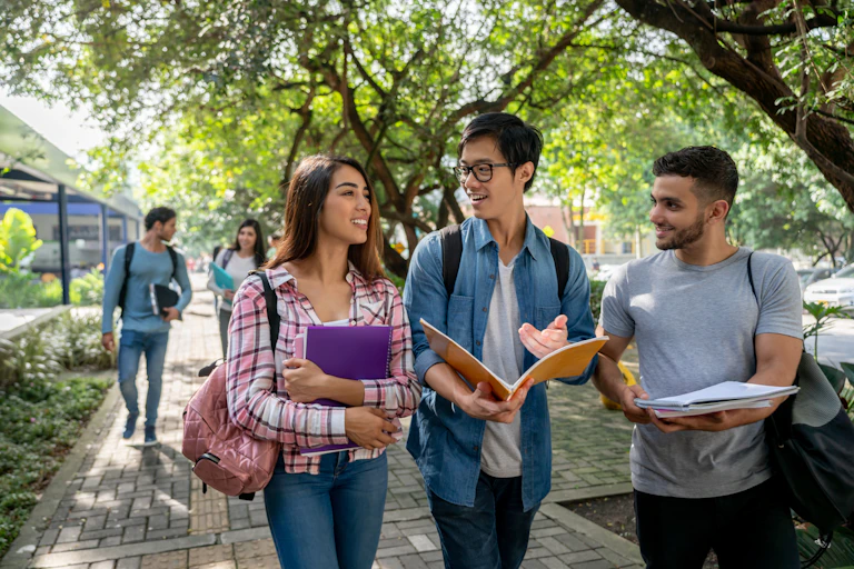 Three college students walk together, each carrying books in their hands.