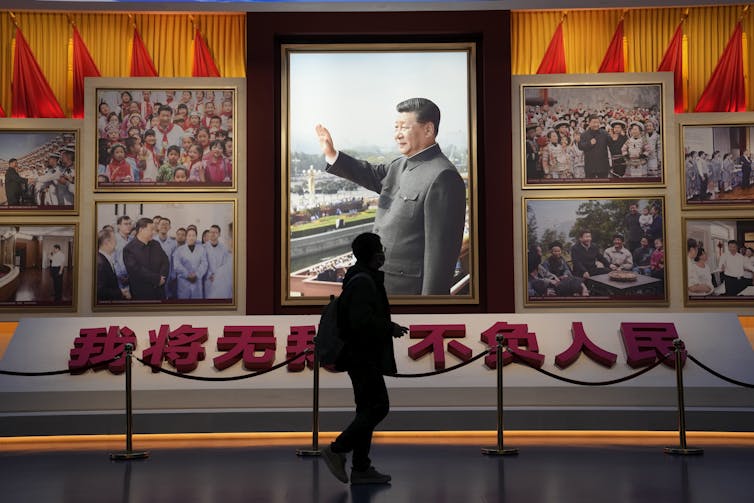 A man in silhouette walks past a photo of Xi Jinping waving.