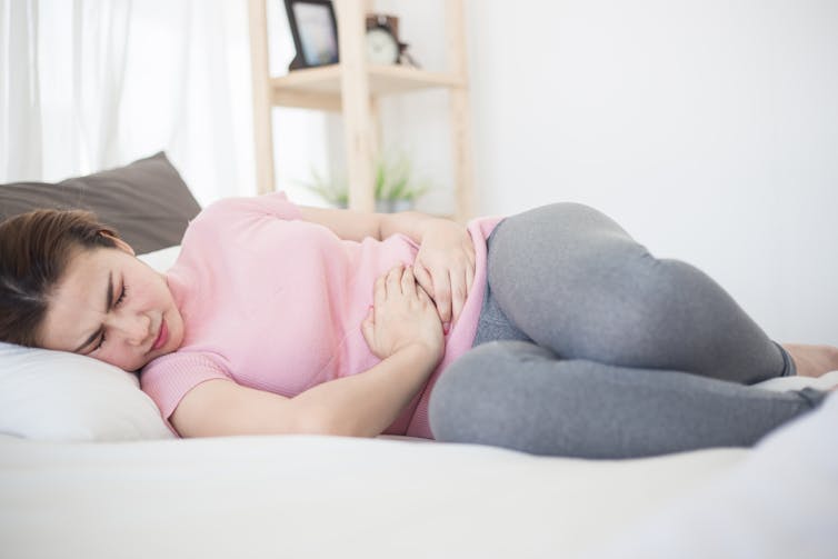 Femme allongée dans un lit se tenant l’abdomen sous la douleur.