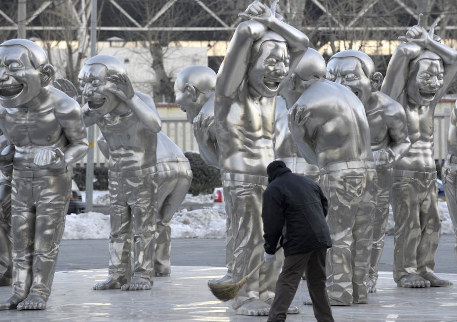 Statues argentées monochromes d'hommes torses nu grimaçant balayées par un homme de dos.