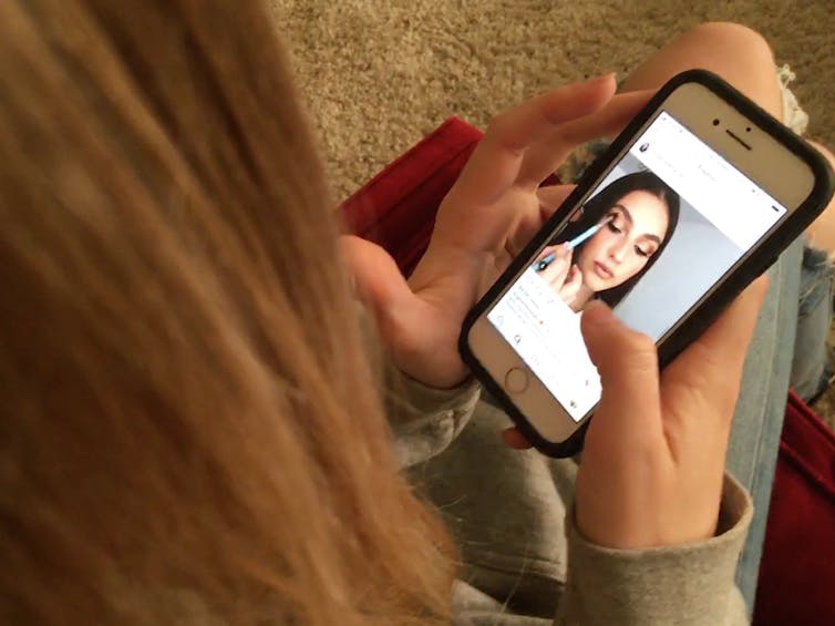 Un adolescente mira una publicación de Instagram de una mujer joven que se maquilla