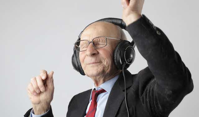 Un vieux monsieur, heureux et plein d'entrain, écoute de la musique un casque sur les oreilles.
