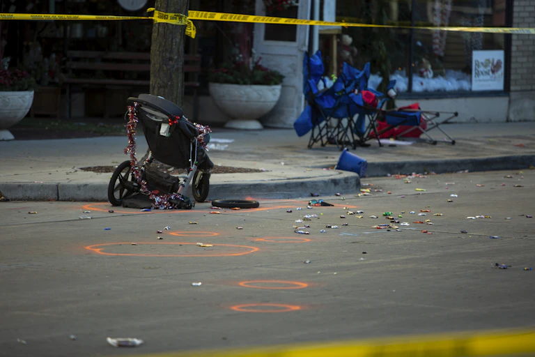 A mangled stroller and camp seats line the street with yellow police tape fluttering above.