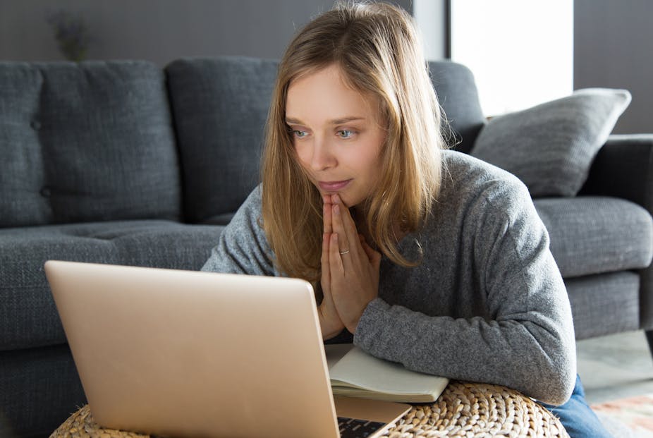 A woman prays in front of her laptop.