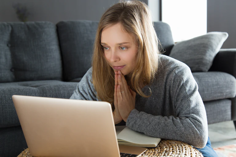 A woman prays in front of her laptop.