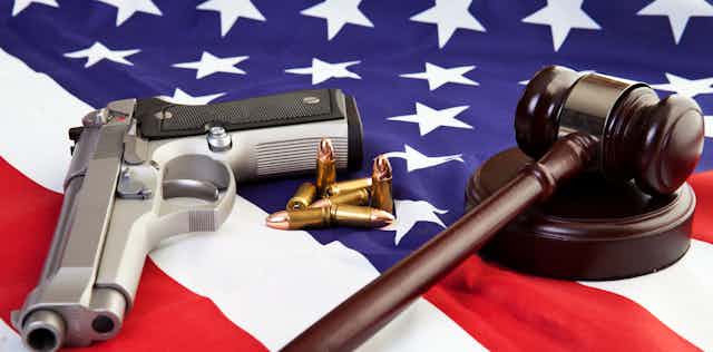 A gavel, gun and bullets are strewn over a US flag.