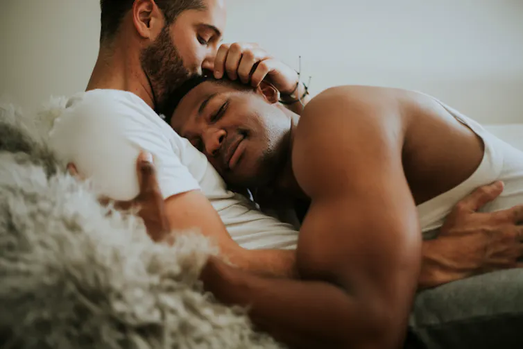 Gay couple cuddle in bed.