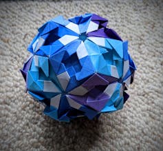 A blue and purple origami shape sits on a grey background.