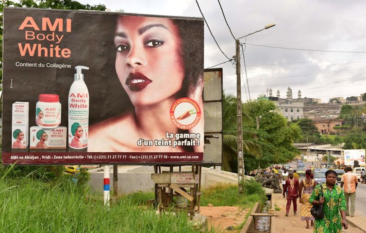 People walk past a billboard with a glamorous-looking woman on it, along with the words 'Ami Body White'