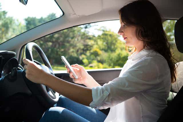 A woman holds her smartphone while driving.