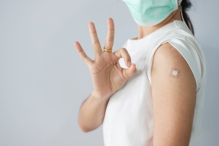 A woman making an 'OK' sign with her hand, having had a vaccine