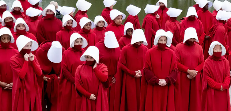 A crowd of women, of white, Black and Asian identities, seen in cloaks and bonnets.