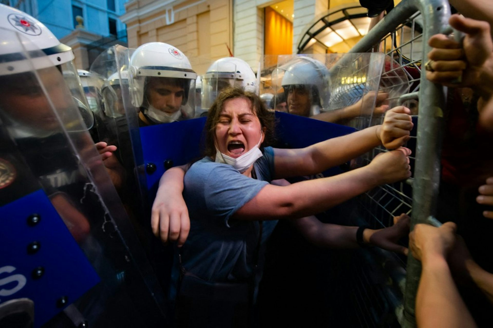 Une femme hurle, encerclée par des policiers antiémeutes et se tenant à une barrière durant une manifestation.