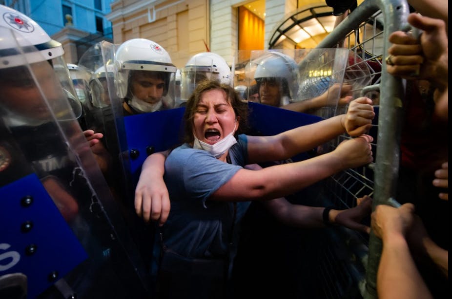 Une femme hurle, encerclée par des policiers antiémeutes et se tenant à une barrière durant une manifestation.