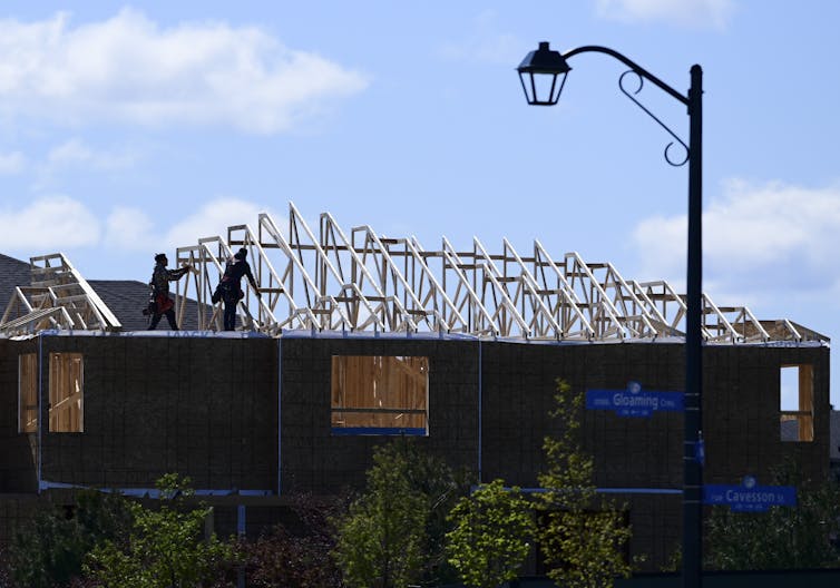 Two construction workers work on the roof of a house being built