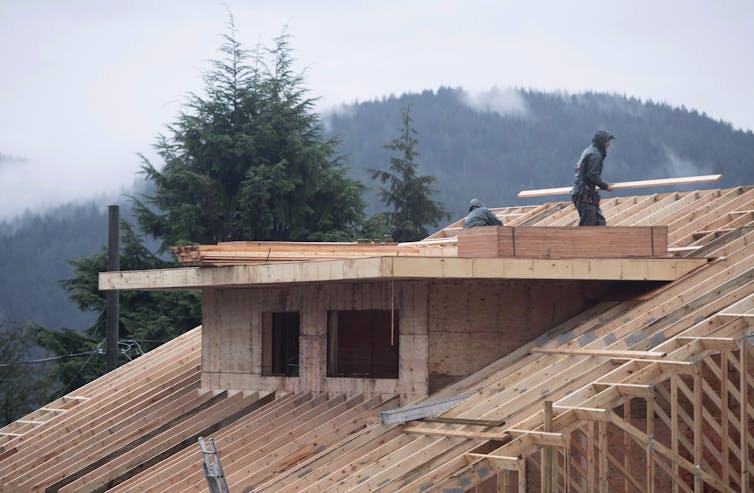 A construction worker carries lumber on the roof of a home mid-build.