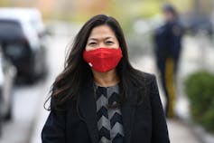 A woman with long dark hair wears a red mask as she walks outdoors.