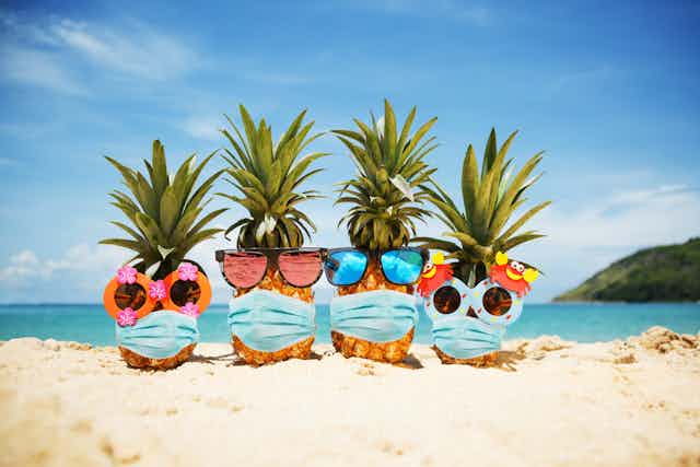 Four pineapples on the beach wearing masks and sunglasses