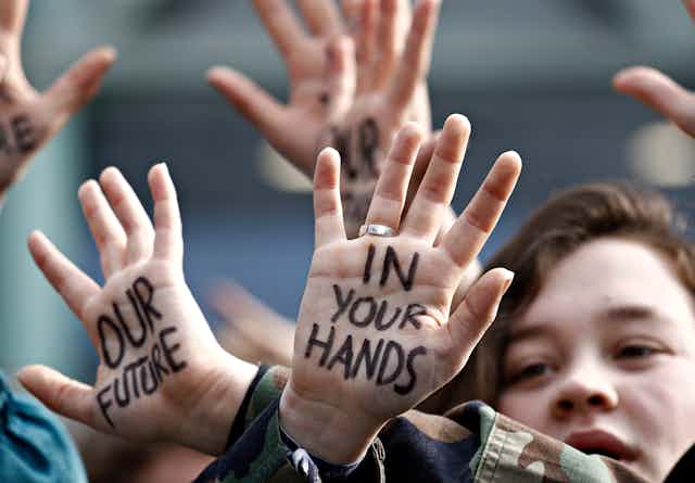 Young people at a climate protest with the words 'Our future in your hands'written on their palms