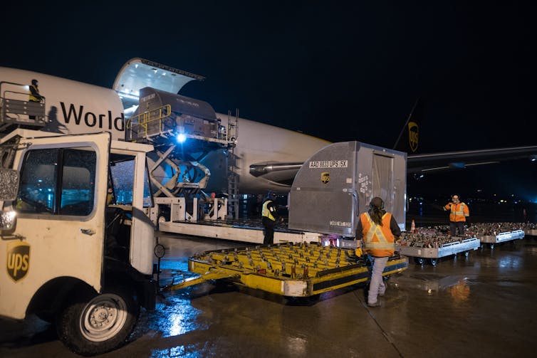 A storage container rolls out of a cargo plane at night