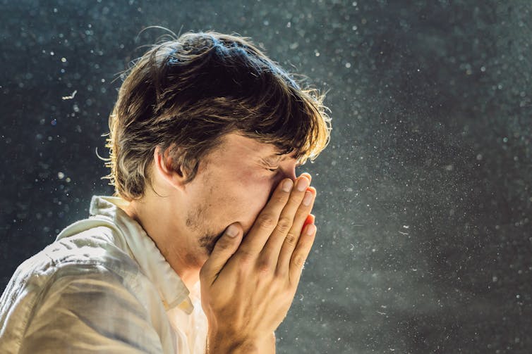 A man sneezes in a dusty room