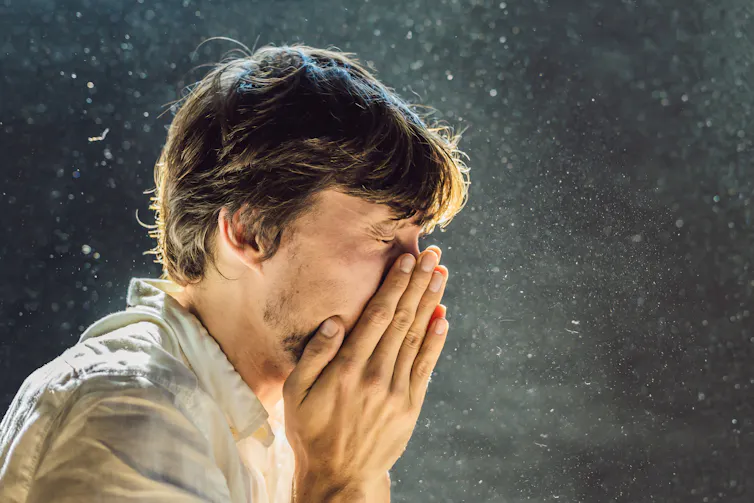 A man sneezes in a dusty room