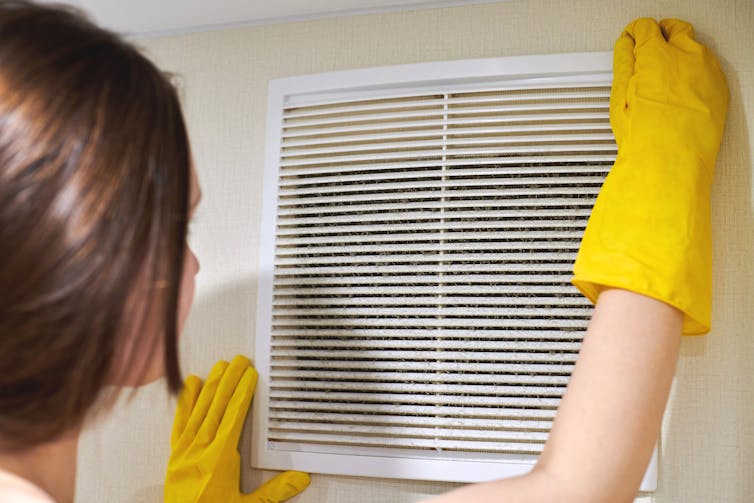A woman cleans a vent.