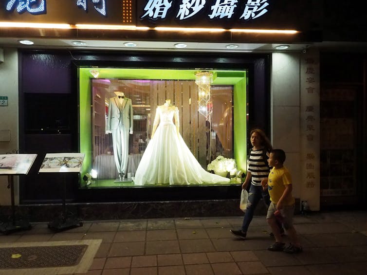 A woman and a boy walk past a wedding photo gallery in Taipei, Taiwan.