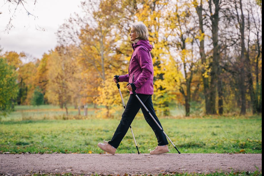 Older woman walking in a park with walking sticks.
