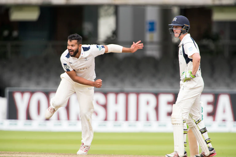 Two men in cricket kit, one in movement after bowling ball