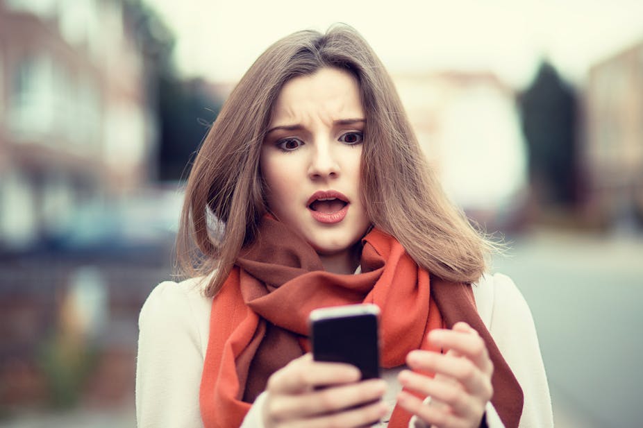 A woman looks in surprise and shock at her mobile phone