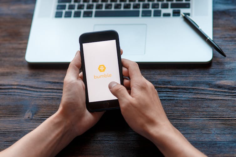 A pair of hands holding a mobile phone with the opening screen of the Bumble app.