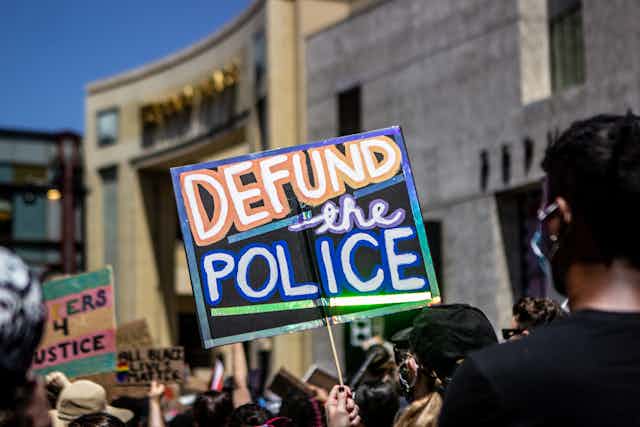 A sign reads 'defund the police' held above protestors heads