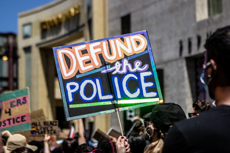 A sign reads 'defund the police' held above protestors heads