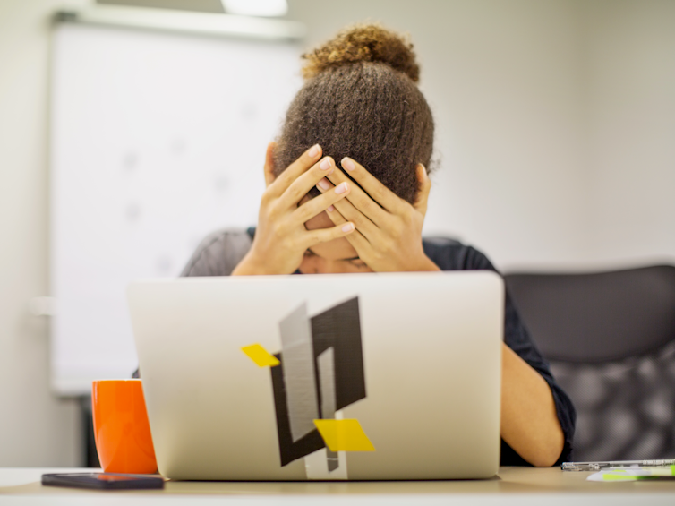 Woman faces her laptop, head in hands.