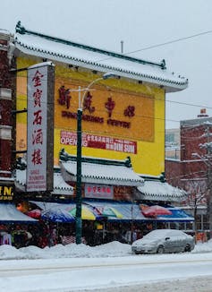 A sign is seen for 'all day dim sum' on the front of a Chinese restaurant amid other signage while it is snowing outside.