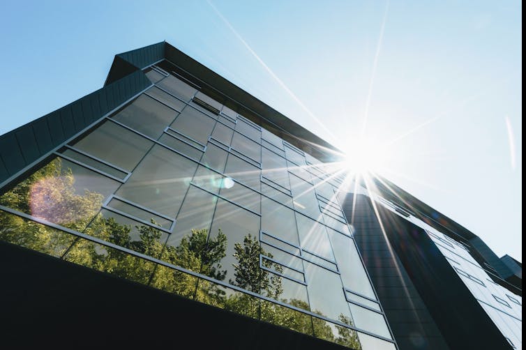 The sun shines over an office building with trees at its base.