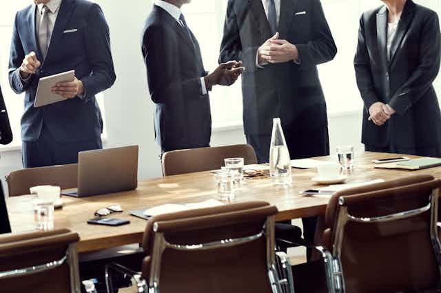 People in suits in discussions as they stand behind a boardroom table