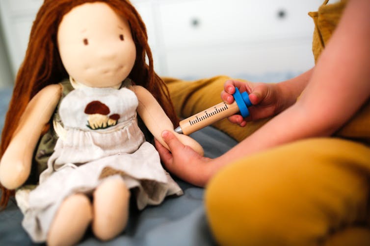 Child practices vaccinating a doll.