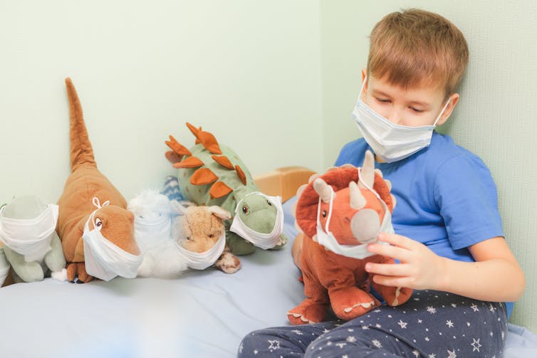 Little boy plays with stuffed toys wearing face masks.