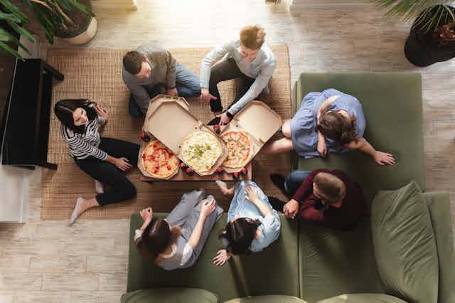 A birds-eye view of a group of young people sitting around some pizzas.