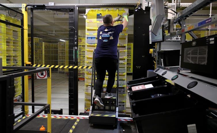 An Amazon worker at a warehouse in Germany loads a rack that is driven by automated robotics.