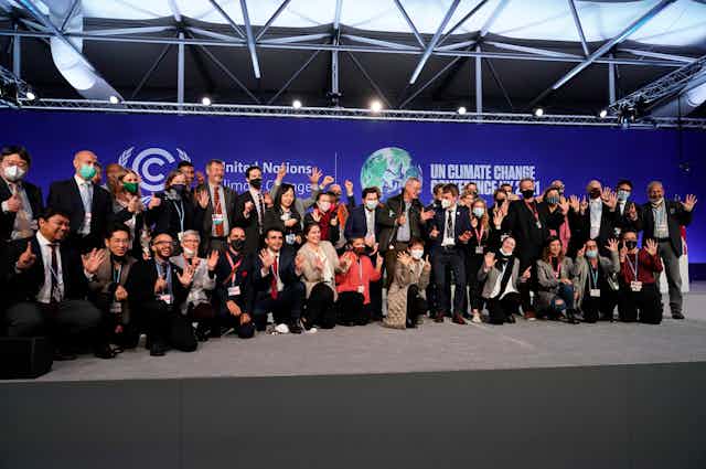A group of people pose in front of a blue backdrop displaying the COP26 logos