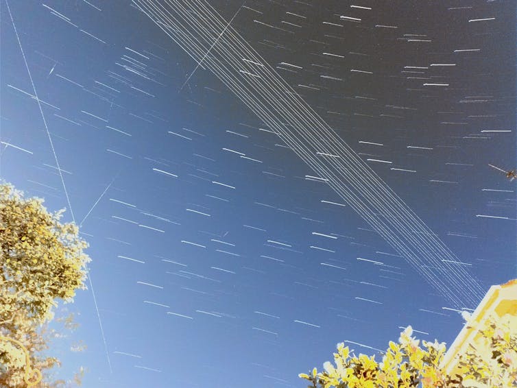 A photo of the night sky showing telegraph cables, trees, and rays of light.