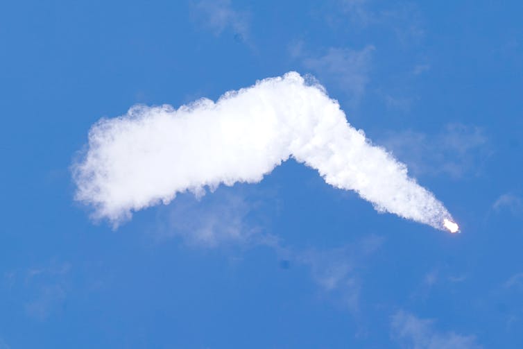A rocket with a large white cloud trail against a bright blue sky
