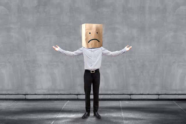 Man with a paper bag over his head with a sad face on it