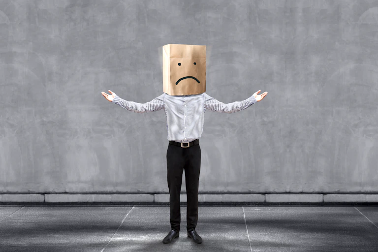 Man with a paper bag over his head with a sad face on it