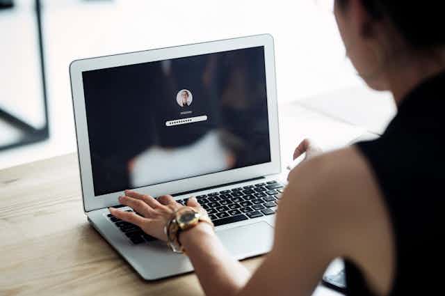A woman types a password on a laptop.