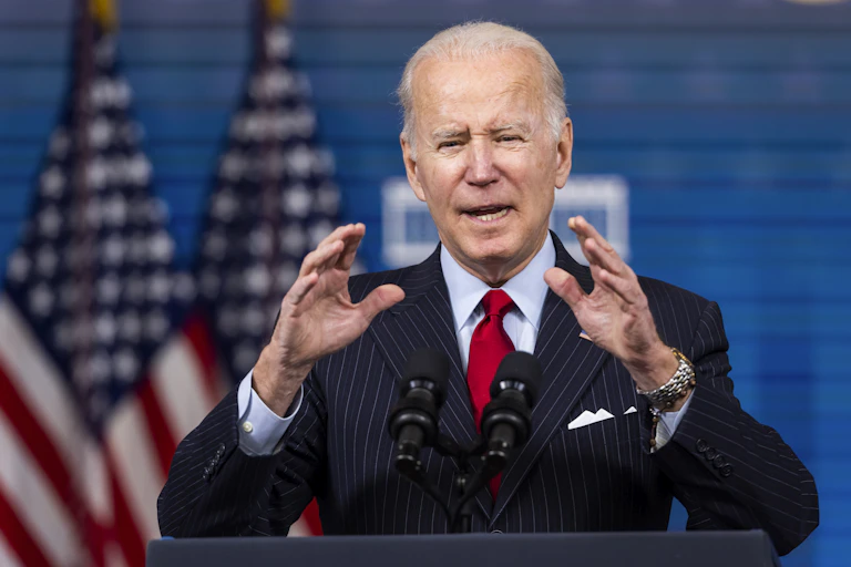 US president Joe Biden makes a speech, gesturing with his hands, with two US flags in the background.