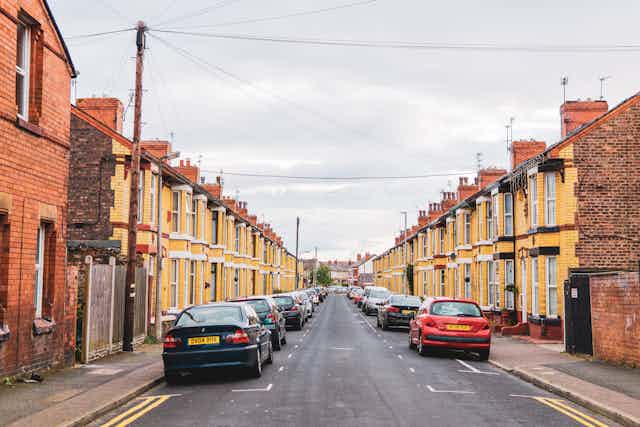 A street of yellow brick terraced houses with cars parked out front.